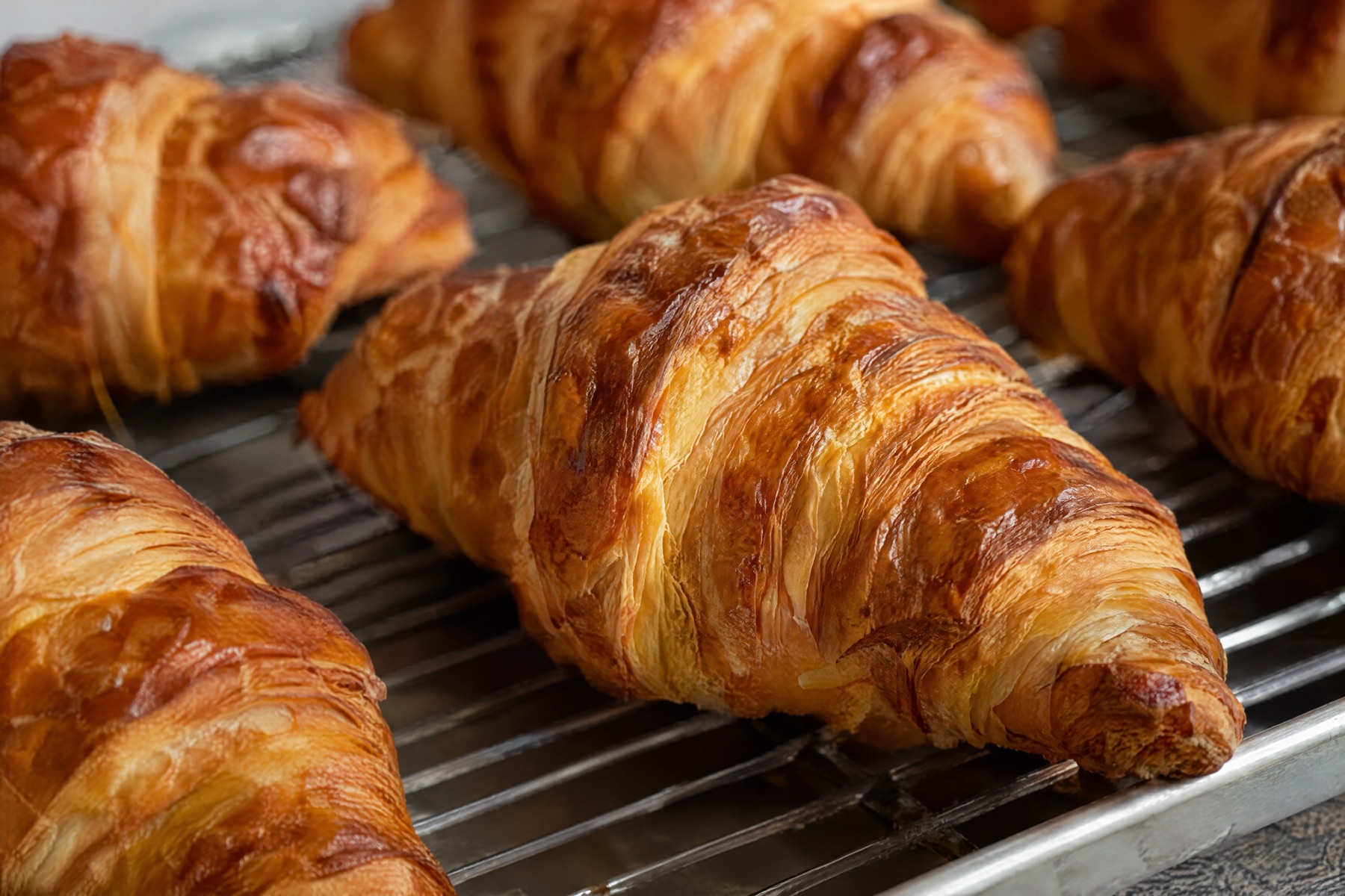 Golden, flaky croissants cooling in rows on a wire rack